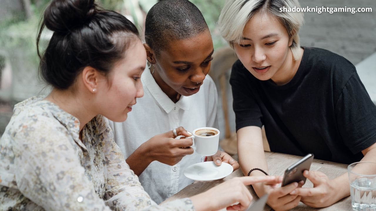 3 girls looking at a phone discussing sitting at a table drinking coffee